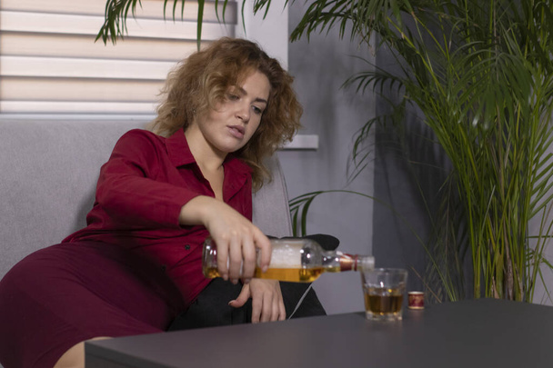 drunk business lady in red blouse and skirt with a bottle and glass of whiskey. hard work. disappointment and sadness - Photo, Image