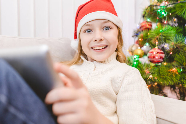 La niña feliz con un sombrero de Santa Claus sostiene una tableta - Foto, imagen