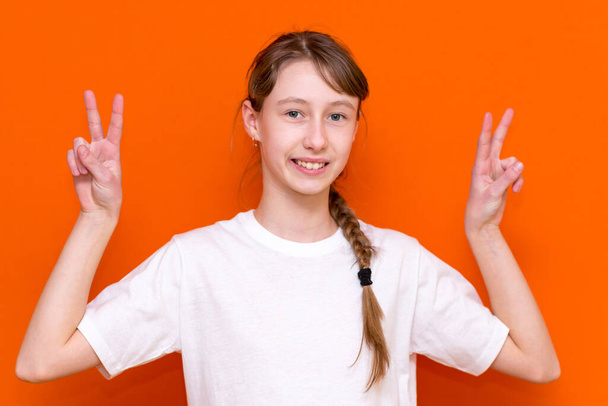 Photo rapprochée de belles petites filles bras montrant signe v symbole dire bonjour amis bonne humeur porter t-shirt blanc sur fond de couleur orange - Photo, image