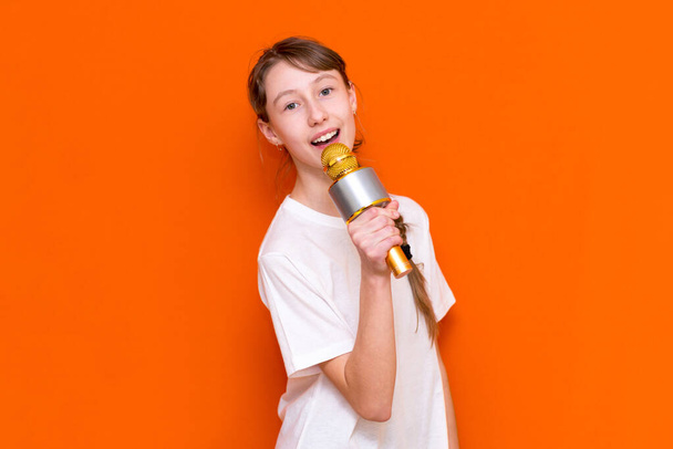 Happy young beautiful girl singing with microphone on orange studio background - Фото, зображення