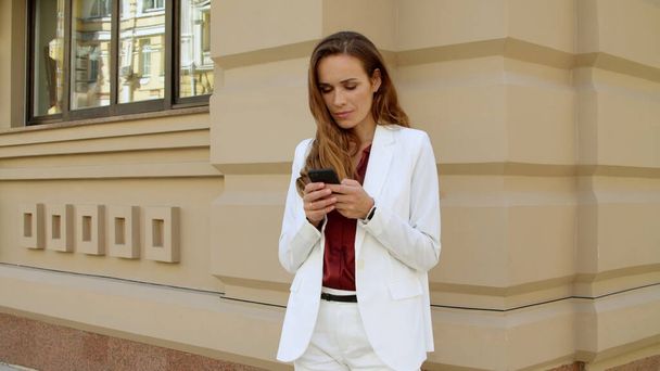 Thinking business woman texting message on mobile phone outdoors - 写真・画像