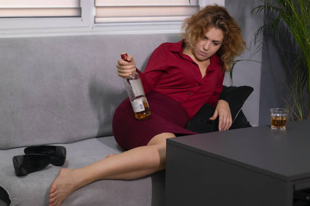 Empresaria borracha en blusa roja y falda con una botella y un vaso de whisky. trabajo duro. decepción y tristeza - Foto, imagen