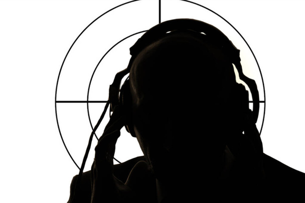 Η σιλουέτα ενός άντρα με ακουστικά στο φόντο του στόχου. Αντίληψη: μυστικός πράκτορας κρυφακούει, κατάσκοπος και ανιχνευτής, είστε κάτω από το όπλο, σκοπευτής ή δικαστής στο σκοπευτήριο. - Φωτογραφία, εικόνα