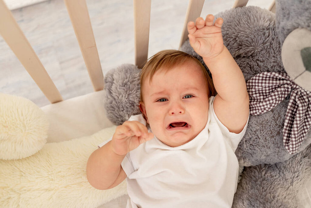 赤ん坊の男の子6ヶ月大きなテディベアと彼のベビーベッドで泣いて - 写真・画像