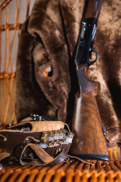 ロッキングチェアのカートリッジベルトと12ゲージ狩猟ライフル。熊の皮はロッキングチェアの後ろにかかっています - 写真・画像