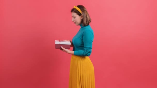 Muotokuva onnellinen nainen avaa lahjapakkauksen punaisella taustalla. - Materiaali, video