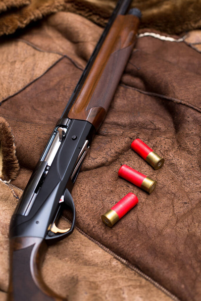 een jachtgeweer en drie rode 12-gauge patronen liggen op de huid van een beer. - Foto, afbeelding