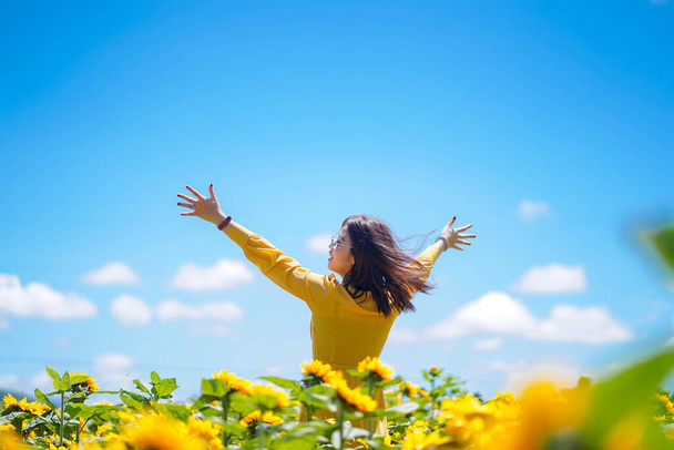 Boldog gondtalan nyári nőt a napraforgó mezőn tavasszal. Vidám, multiracionális ázsiai nő, felemelt karokkal mosolyog..  - Fotó, kép