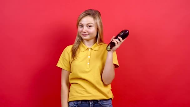 Menina bonito e ligeiramente gordo em uma camiseta amarela segurando berinjelas frescas em sua mão, - Filmagem, Vídeo