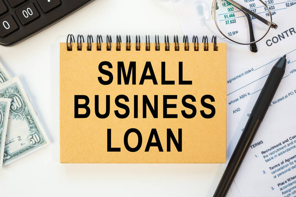 SMALL BUSINESS LOAN is written on a notepad, on an office desk with office accessories. Business concept. - Foto, afbeelding