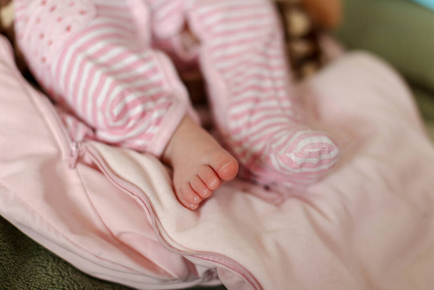 The baby's bare leg protrudes from a pink striped jumpsuit - Foto, Imagem