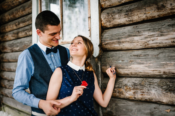 Romantic couple on valentine's day. Man hug a woman in back against the backdrop of a wooden wall of the house. Heart hanging around on body. close up. love story concept. - Photo, image