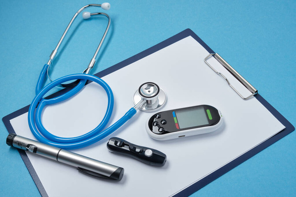 clipboard with white blank sheets of paper, stethoscope, glucose meter, lancet and syringe pen with insulin on blue background, daibet day concept, diabetes diagnostics - Foto, Imagem