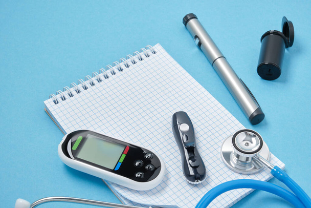 clean block with spring, stethoscope, glucose meter, lancet and syringe pen with insulin on a blue background, daibet day concept, diabetes diagnosis - Photo, image