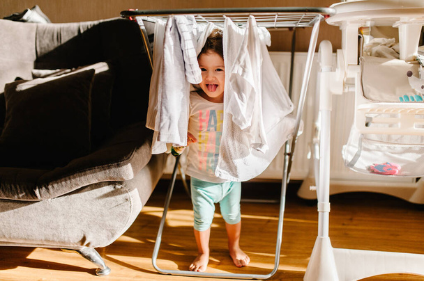 Portrait of a little, pretty, cute, toddler, girl, adorable baby, hangs laundry on clothesline and play on floor at home. - Valokuva, kuva