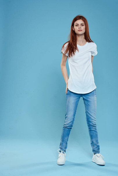 Beyaz tişörtlü, mavi kot pantolonlu, tam gelişmiş stüdyo mavi arka planlı güzel bir kadın. - Fotoğraf, Görsel