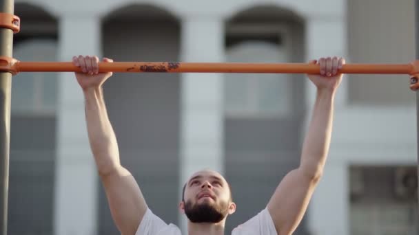 Мускулистый мужчина подтягивается на горизонтальной полосе. на тренировочной площадке рядом с домом - Кадры, видео
