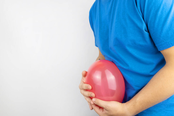 Nadýmání a nadýmání. Muž drží červený balón poblíž břicha, což symbolizuje problémy s plynem. Střevní trakt a trávicí ústrojí - Fotografie, Obrázek