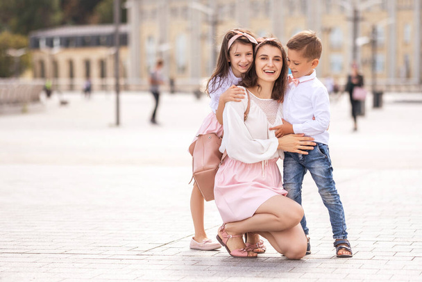 Young cheerful mom with kids on a walk in european city. Kids smiling and having fun. Summer portrait with space for text. - Fotó, kép