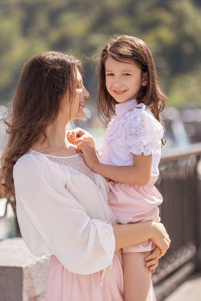 Young cheerful mom with daughter on a walk in european city. Little girl smiling and having fun. Summer portrait with space for text. - 写真・画像