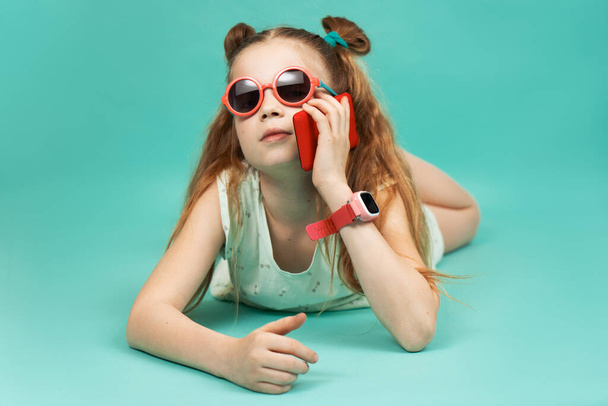 Bright colors: a girl in sunglasses lies on her stomach and talks on a smartphone. - Foto, Imagem