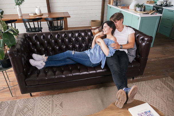 Loving couple in casual outfit laying on a sofa in their home. They cuddling, relaxing happily, hugging each other. - Foto, immagini