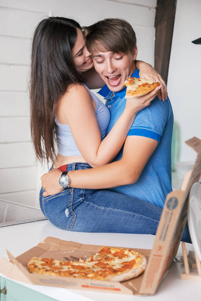 Young couple in love eating pizza at their kitchen. Cozy relaxing portrait of weekend leisure. - Photo, Image