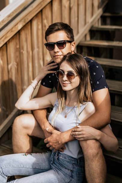 Blisko romantycznej pary w embrance odwróć wzrok. Szczęśliwy mężczyzna i kobieta siedzą na drewnianych schodach - Zdjęcie, obraz