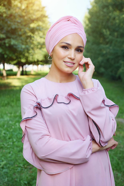 Красивая мусульманка в розовом платье и тюрбан на фоне зеленых деревьев - Фото, изображение