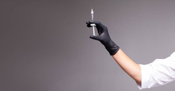 Kéz a kézben fekete kesztyű tartó fecskendő fénymásoló. Fecskendő éles tűvel a kezében. Orvosi kezelési koncepció. Laboratóriumi háttér. Orvosi fogalom. Védőoltás fogalma. - Fotó, kép
