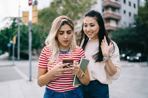 Multiracial hipster girls enjoying mobility chatting and messaging during city sightseeing on vacations, charming female bloggers using smartphone for making online booking and travel ticketing - Foto, immagini