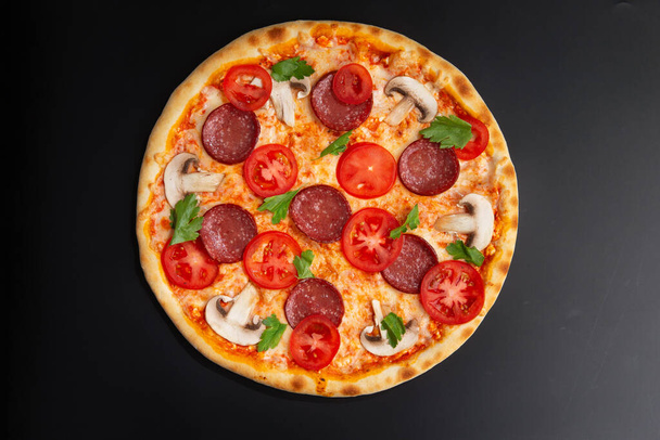 pizza with tomatoes, pepperoni and herbs on a black background - Photo, Image