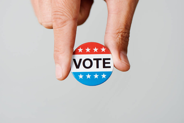 close-up de um jovem caucasiano com um crachá de voto para a eleição dos Estados Unidos em sua mão, em um fundo esbranquiçado com algum espaço em branco - Foto, Imagem