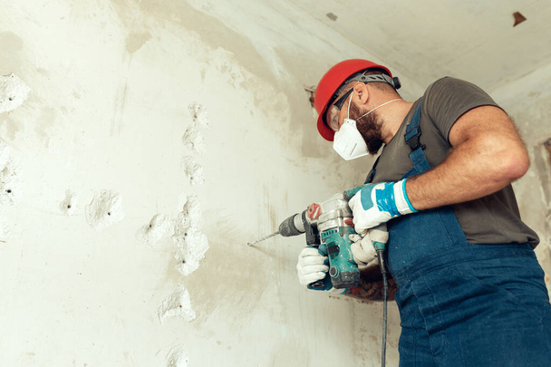 Beton duvarda delik açan inşaatçı koruyucu kostüm ve kask giymiş. - Fotoğraf, Görsel