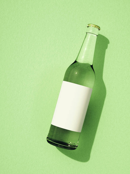 One closed transparent glass beer bottle laying on light green surface. Bottle with blank white label, shadow on background. Retro drink bottle concept. - Фото, зображення