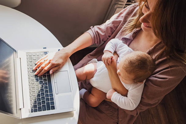 Young mom working remotely on laptop while taking care of her baby. - Valokuva, kuva