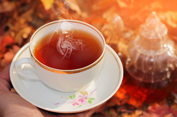 una tazza di tè in mano nei raggi di luce intensa sullo sfondo delle foglie autunnali. - Foto, immagini