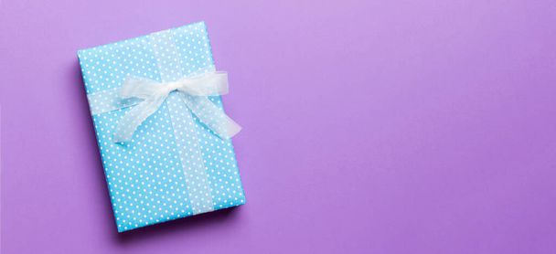 verpackte Weihnachten oder andere Feiertage handgemachtes Geschenk in Papier mit weißem Band auf lila Hintergrund. Geschenkschachtel, Geschenkdekoration auf farbigem Tisch, Draufsicht mit Kopierraum. - Foto, Bild