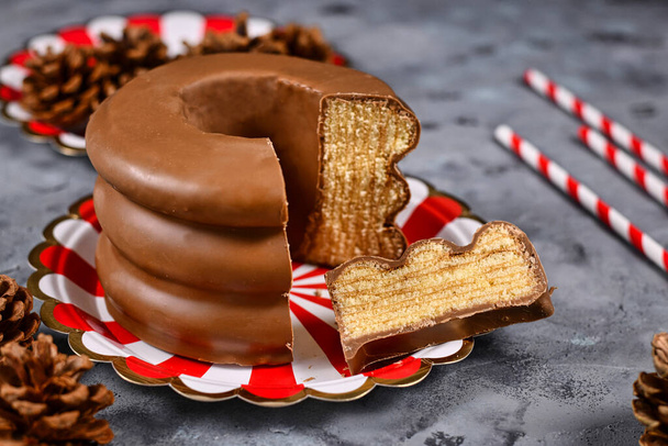 Cut open traditional German layered winter cake showing layers inside called 'Baumkuchen' glazed with chocolate, surrounded by seasonal decoration - Foto, Imagen