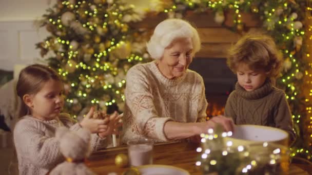 居心地の良いセーターで子供たちのショット映像のシーケンス祖母のパックの贈り物を助けクラフト紙を粉砕し、リボン弓を結ぶおもちゃのクリスマスボックスを飾る - 映像、動画