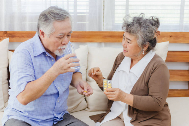 Asian couple woman caring sick elderly man by giving pill or drug at home. Love and relationship of retired senior couple. Health care and medicine of illness aged people photo concept. - Photo, Image