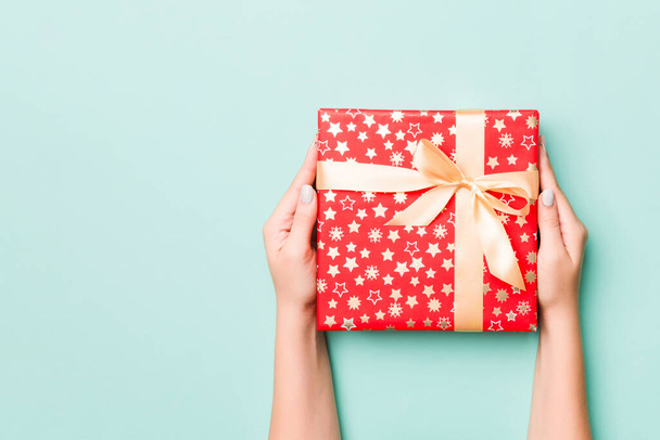 Női kéz ad csomagolt karácsony vagy más ünnep kézzel készített ajándék színes papírba. Ajándék doboz, ajándék dekoráció a kék asztalon, felülnézet másolási hellyel. - Fotó, kép