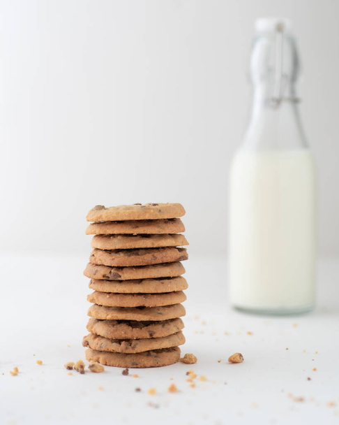 A vertical shot of a stack of chocolate chip cookies and a bottle of milk in the background - 写真・画像
