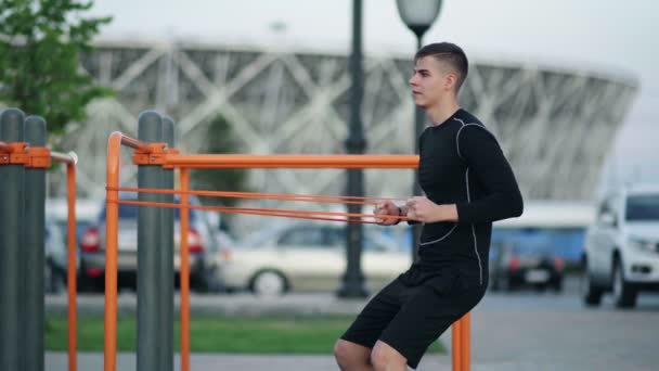 Homem jovem muscular fazendo exercícios com banda elástica ao ar livre. Exercício - Filmagem, Vídeo