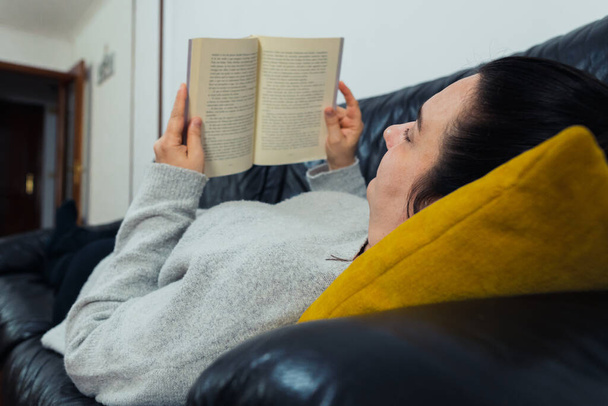 Uma mulher lendo um livro enquanto deitada no sofá - Foto, Imagem