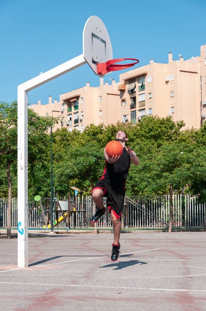 A vertical shot of a young man throwing ball into the basketball basket - 写真・画像