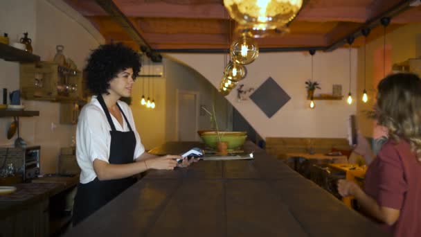 Contactloze betaling met mobiele telefoon aan de balie van een restaurant. Jonge vrouwelijke klant met smartphone voor contactloze betaling in coffeeshop. - Video