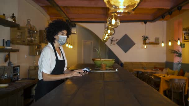 Bir restoranın tezgahında cep telefonu kullanarak gizli kodlu bir ödeme yapılmış. Garson ve müşteri koruyucu yüz maskesi takıyor. Covid-19 salgınından sonra yeni normal. - Video, Çekim