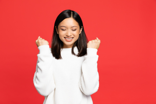 young asian woman with closed eyes rejoicing and smiling isolated on red  - Foto, immagini