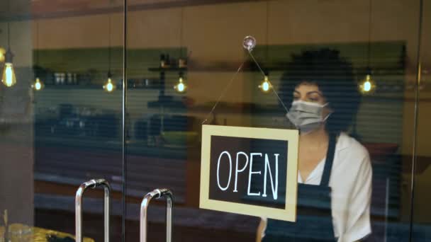 ビジネスウーマンは、 covid-19の流行により事業活動を終了しました。外科マスクを持つ所有者は、コロナウイルスの隔離のためにレストランのドアに閉鎖的な兆候を置きます。COVID-19危機コンセプト. - 映像、動画